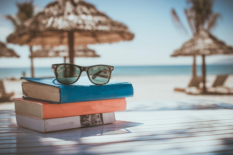 Summer-themed picture of books near a beach Summer-themed picture of books near a beach