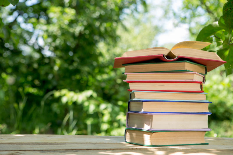 Pile of books amidst a summery garden backdrop Pile of books amidst a summery garden backdrop