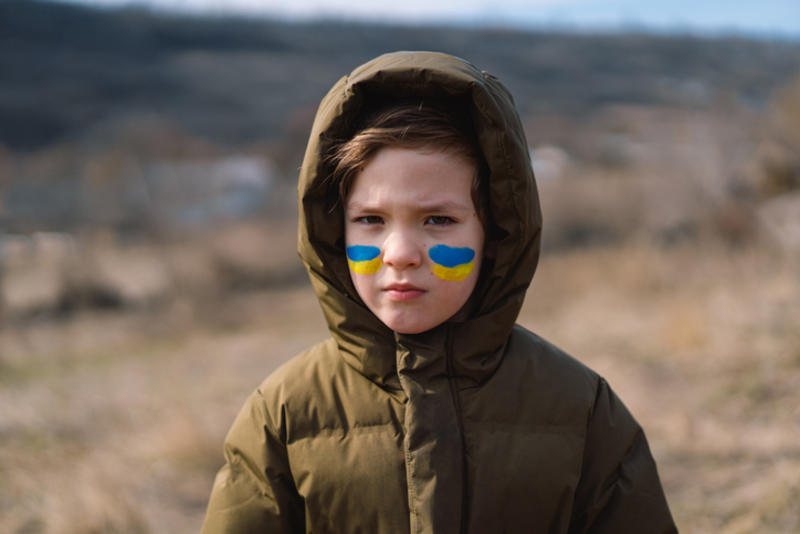 Young girl stares into the camera with Ukrainian flag colours painted on her cheeks