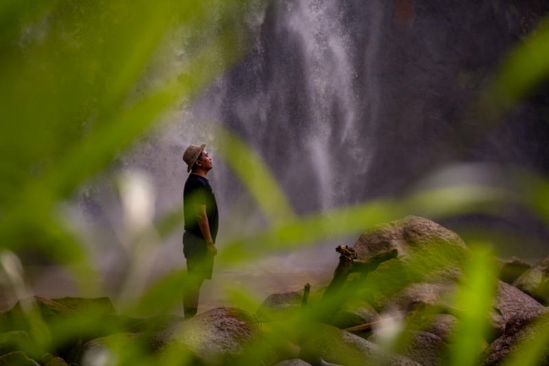 A man stands on a rock by a waterfall