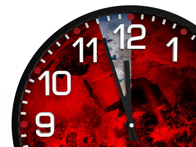 An analogue clock showing 11.57, with the three minute before midnight in bluey-grey, and the rest coloured in red with clouds in the backgroundstock