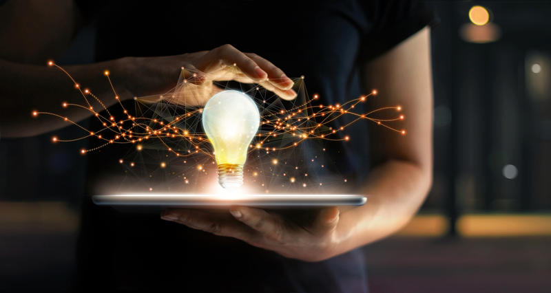 Lightbulb Moment IP creativity A person holding a tablet, with a lit-up lightbulb balanced on top with bright electrical currents flowing around it.
